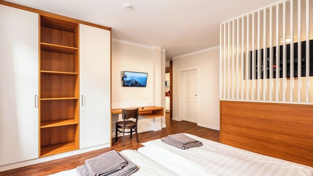 A hotel room with two beds, a desk, a chair, a TV, and a wardrobe.