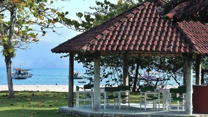 A gazebo with a tiled roof overlooking a beach with boats. - Pousada Tarituba (Paraty)