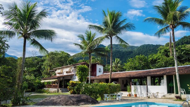A pool area with a clear view of a house, surrounded by palm trees and greenery. - Pousada Tarituba (Paraty)