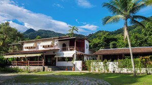 A two-story house with a balcony, surrounded by lush greenery and a palm tree. - Pousada Tarituba (Paraty)