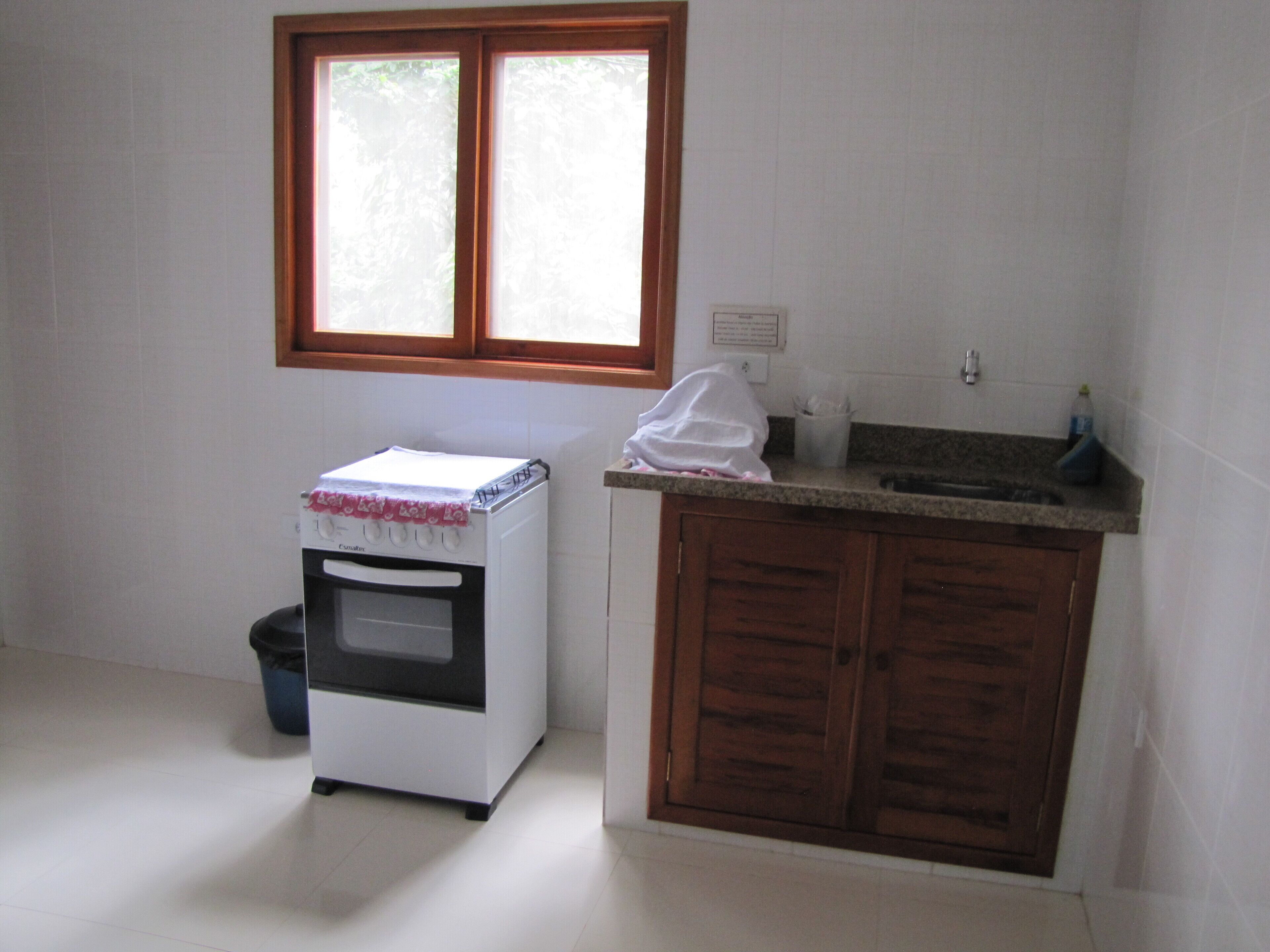 Una cocina pequeña con horno blanco, un gabinete de madera y una ventana sobre el lavadero.