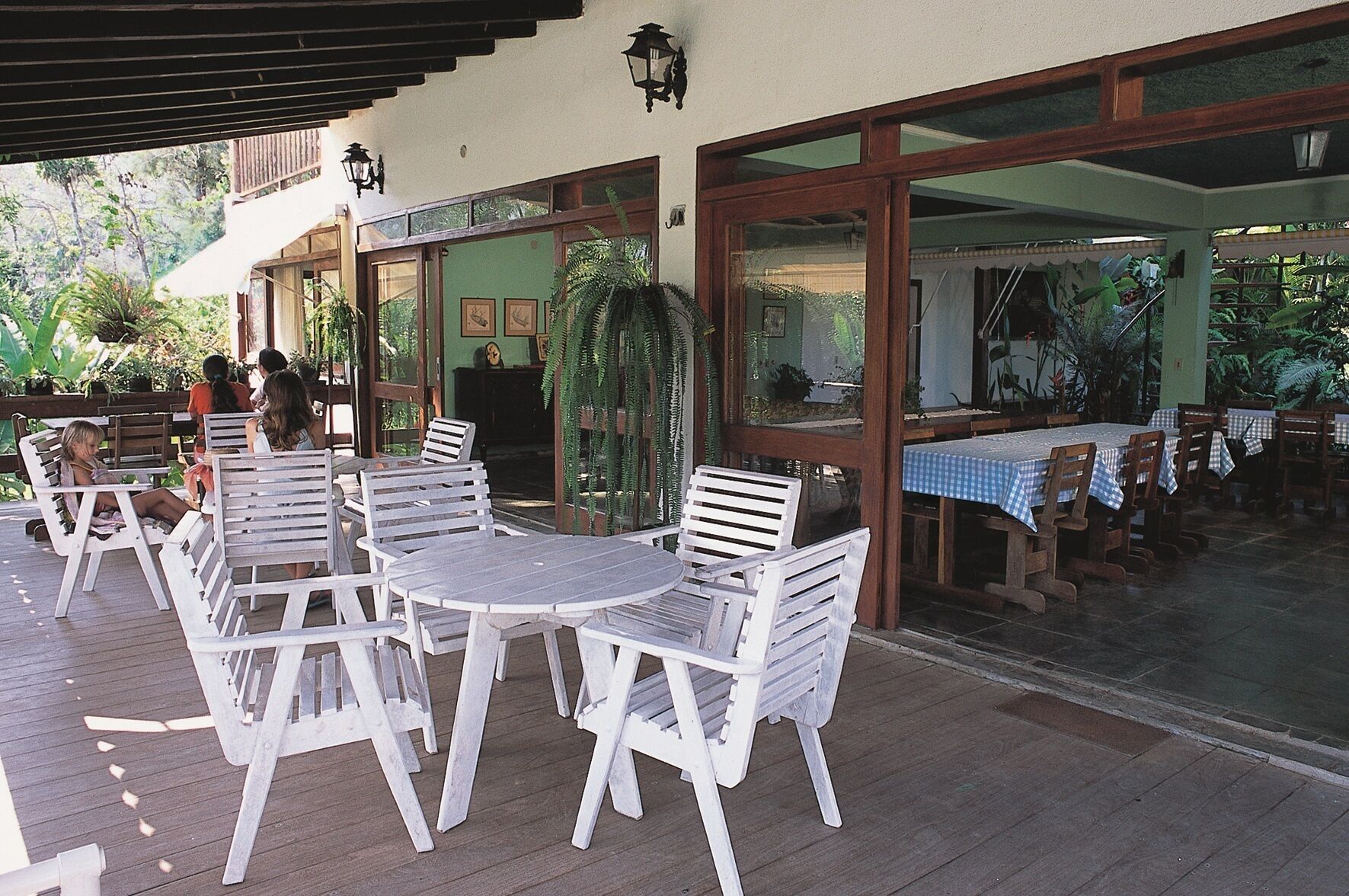 A covered outdoor seating area with white plastic chairs and tables, surrounded by glass doors and windows.