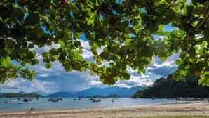A beach with boats on the water, a sandy shore, and a mountainous backdrop. - Pousada Tarituba (Paraty)