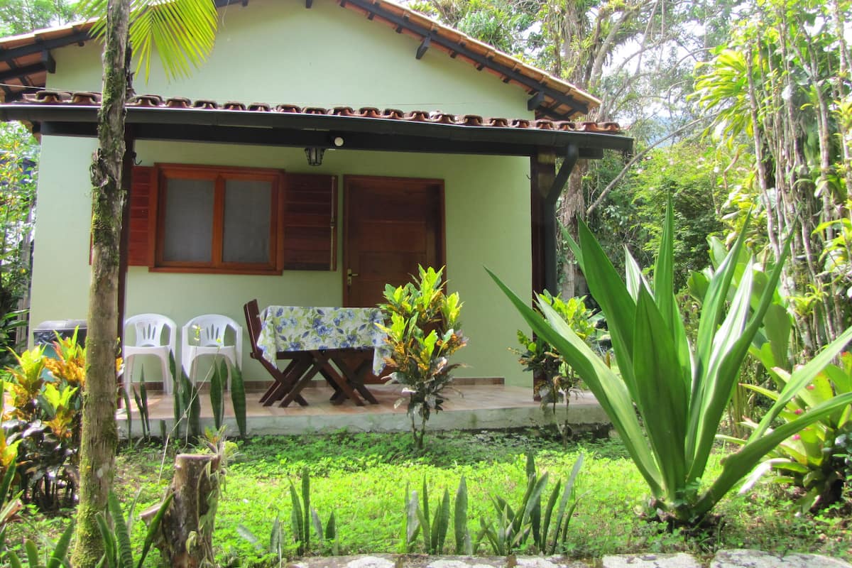 A house with a tiled roof, a porch with a table and chairs, and a garden with various plants.