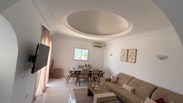 A living room with a sofa, coffee table, TV, dining table, chairs, and a ceiling with a recessed area. - Villa mayline (Arkou)