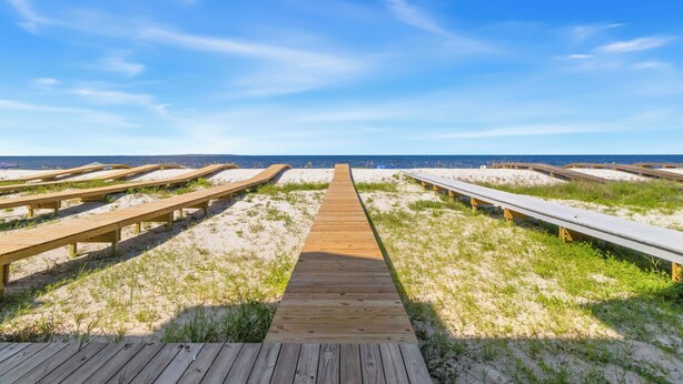 Een houten looppad dat naar een strand leidt, onder heldere luchten.