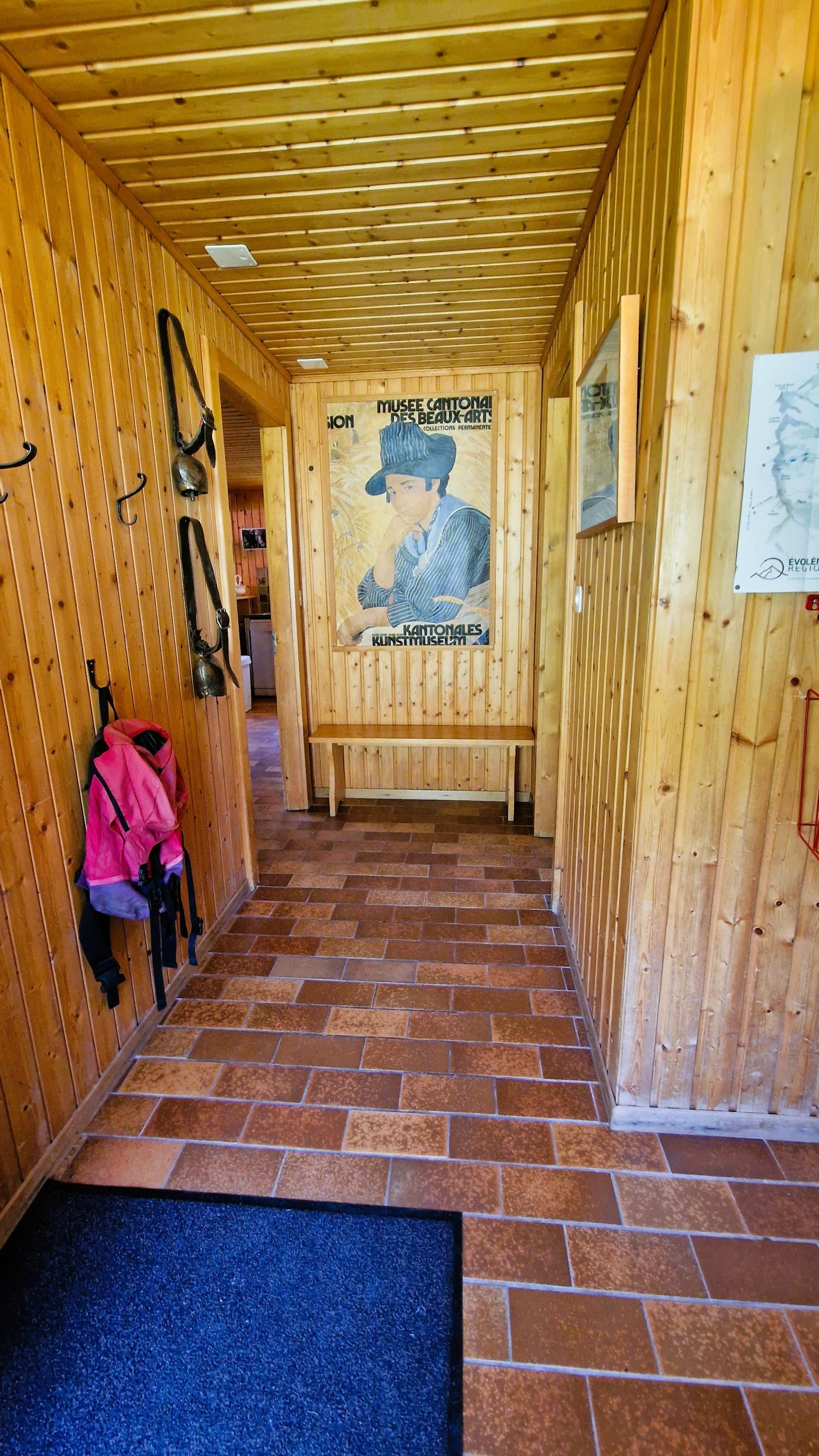 Un couloir en bois avec un banc, une affiche et un tapis bleu à l’entrée.