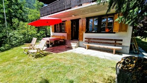 A chalet with a wooden deck, outdoor seating, and a red umbrella.