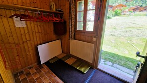 A small room with wooden walls, a radiator, a window with curtains, and a door leading outside.