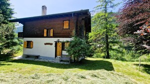 Una casa de madera rústica con fachada blanca, una chimenea y un pequeño porche.