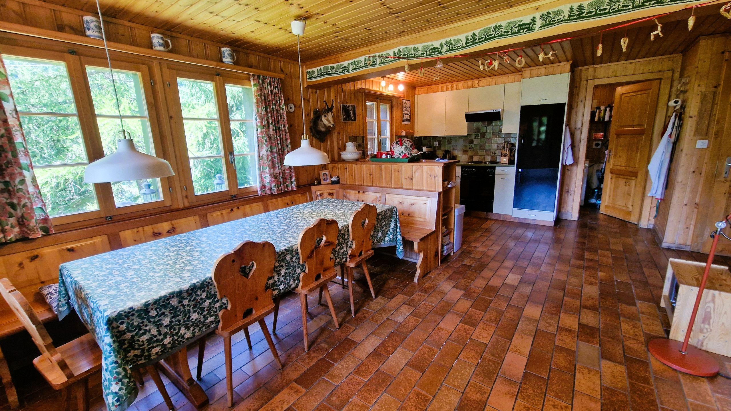 A wooden cabin with a dining area, kitchen, and a large window.