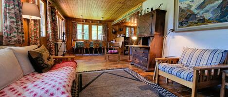 A cozy cabin interior with a wooden ceiling, a sofa, a chair, a dining table, and a fireplace.