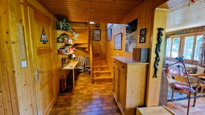 Interior de una cabaña de madera con escalera, estanterías, chimenea y un telescopio.