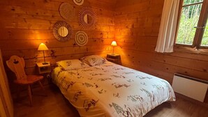 A cozy wooden cabin bedroom with a bed, two bedside lamps, a chair, and a window with curtains. - Chalet Dar El Jebel - 6 personnes (Evolène)
