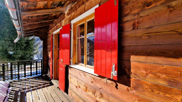 A wooden cabin with red shutters, a wooden deck, and a metal railing. - Chalet Dar El Jebel - 6 personnes (Evolène)