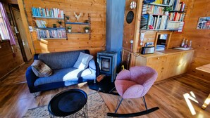A cozy cabin interior with a sofa, a rocking chair, a bookshelf, and a wood stove. - Chalet Dar El Jebel - 6 personnes (Evolène)