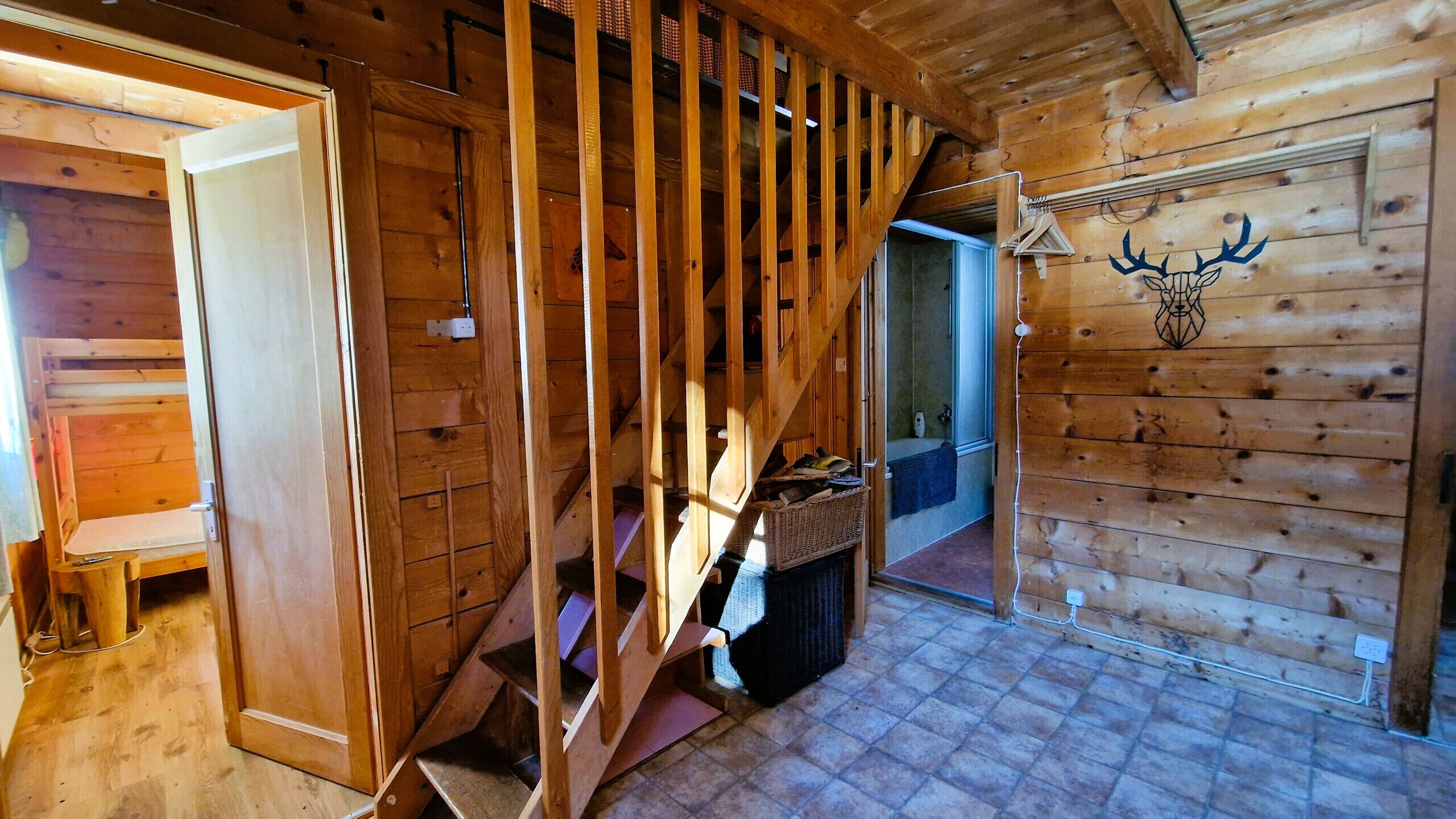 Un interno in legno con una scala, una testa di cervo appesa al muro e un bagno visibile attraverso una porta aperta.