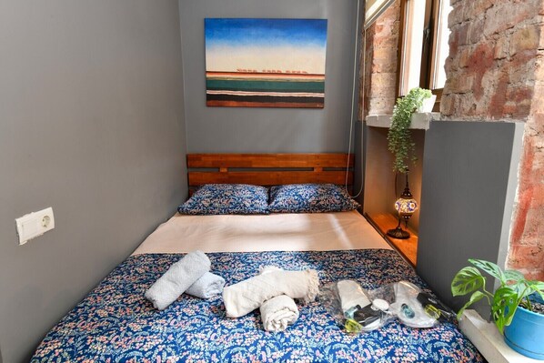 Une chambre à coucher avec un lit en bois, une literie à motifs floraux, un tableau au mur et une plante en pot.