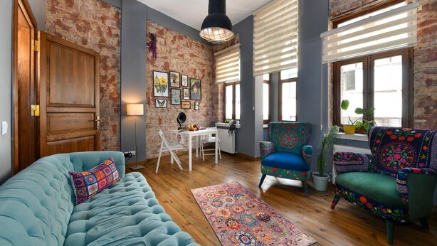 Una sala de estar acogedora con un sofá azul, un sillón estampado y una zona de comedor con mesa y sillas.