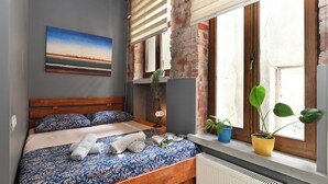 Un dormitorio con una cama de madera, un cuadro en la pared y dos plantas en macetas junto a la ventana.