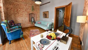 Un salón acogedor con pared de ladrillo, un sofá azul, un sillón estampado y una mesa de comedor con frutas y una copa de vino.
