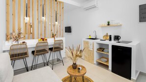 Eine moderne Küche mit Holztrennwand, einem Essbereich mit Korbstühlen und einem kompakten Kühlschrank.