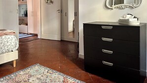 A bedroom with a black dresser, a mirror, a floral rug, and a door leading to another room. - Beautiful air-conditioned apartment a few meters from the center and tram stop. (Firenze)