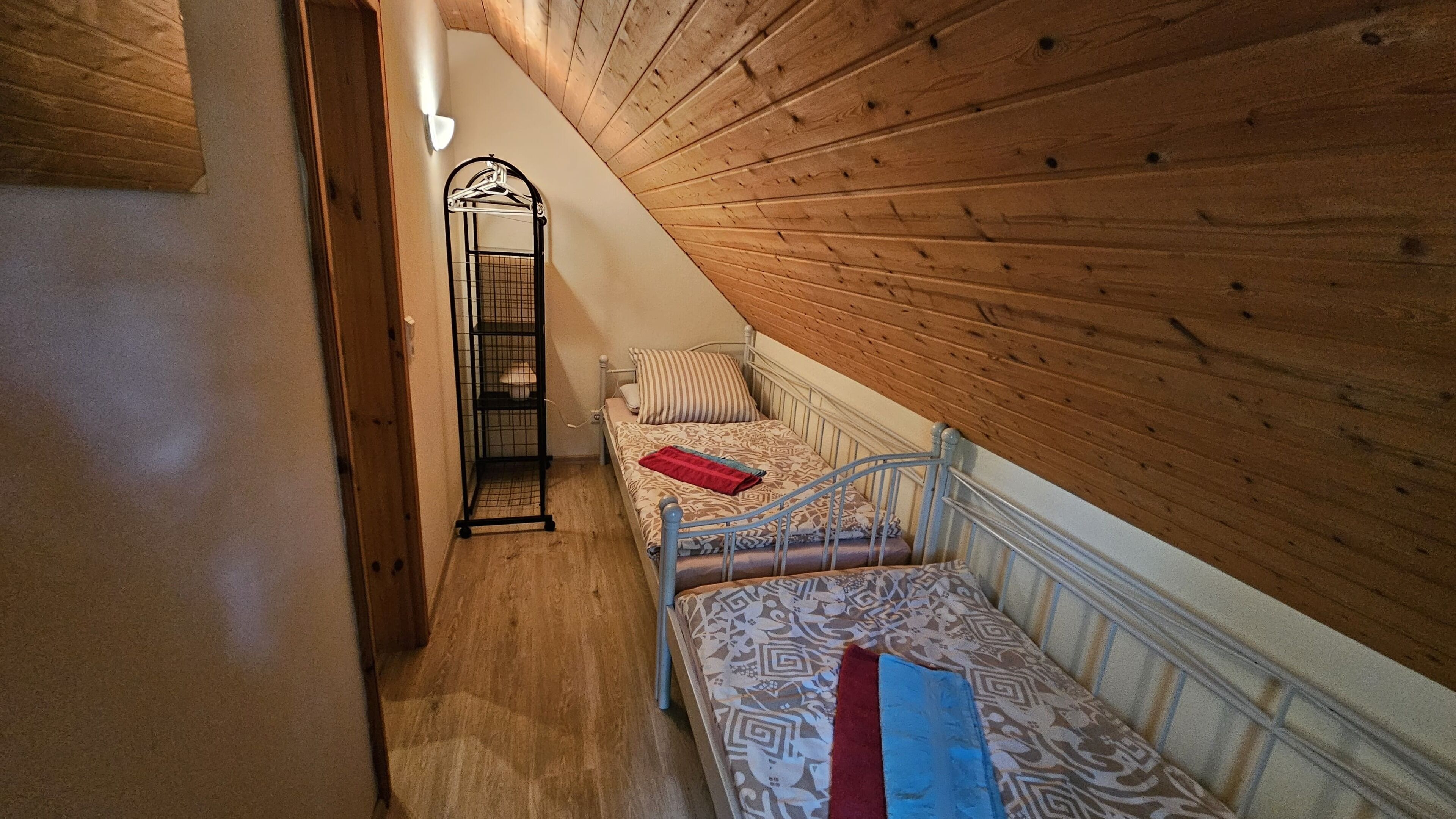 A narrow staircase leading to a loft bedroom with a sloped ceiling, a metal bed frame, patterned bedding, and a hanging clothes rack.