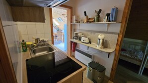 A compact kitchen with a sink, stove, and shelves with kitchenware. - Cozy vacation apartment in the middle of nature, with terrace and barbecue area (Hinzenhagen)