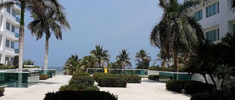 Un patio de hotel con palmeras, piscina y vista despejada al océano.
