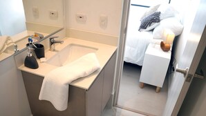 A modern bathroom with a sink, mirror, and toilet. A towel is draped over the sink, and there is a small bedside table with a lamp next to the bed. - Luxury Entire 2 BR Condo Oceanfront In Cartagena (Cartagena)