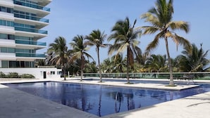 A swimming pool with palm trees, a modern building, and a clear sky. - Luxury Entire 2 BR Condo Oceanfront In Cartagena (Cartagena)