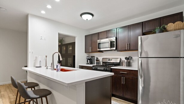 A modern kitchen with a central island, dark wooden cabinets, stainless steel appliances, and a white countertop. - East Side #212 xxxxxxx (Austin)