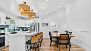 Une cuisine moderne avec des meubles blancs, un îlot central, des tabourets de bar et une table à manger avec des chaises.