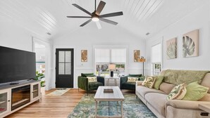 Un salon spacieux doté d’un ventilateur de plafond, d’un téléviseur à écran plat, d’un canapé, d’une table basse et d’une porte donnant sur une autre pièce.