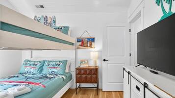 A compact bedroom with a bunk bed, a bedside table with a lamp, a TV, and a door with a palm tree decoration.