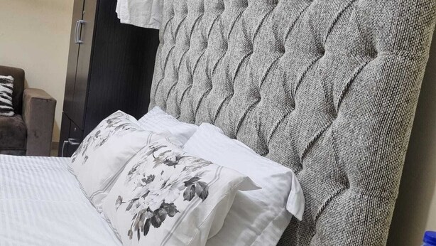 Una cama con cabecera capitonada, un armario de madera oscura y una mesita con estampado de mármol.