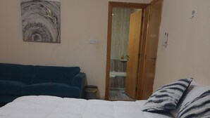Un dormitorio con una cama, un sofá azul y un baño a la vista a través de una puerta abierta.