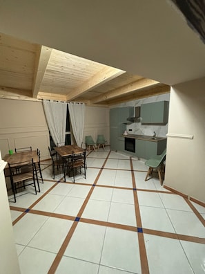 A compact kitchen with a dining area, featuring a tiled floor with a geometric pattern, wooden ceiling beams, and a small countertop with a sink.