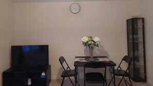 Un salon équipé d’un téléviseur à écran plat, d’une table à manger avec des chaises, d’un vase rempli de fleurs et d’un meuble.