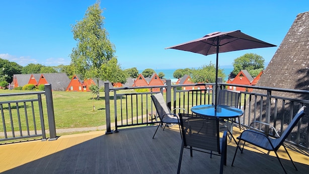 Een houten terras met een tafel en stoelen, een paarse parasol en gebouwen met rode daken op de achtergrond.
