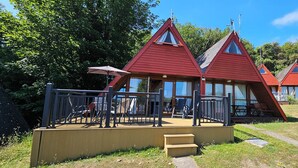Een rij rode chalets met een houten terras en een kleine trap naar de ingang.
