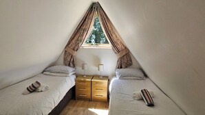 Een kleine, driehoekige kamer met twee eenpersoonsbedden, een houten dressoir en een raam met gordijnen.