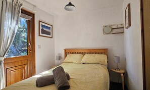 A bedroom with a wooden bed, two pillows, a bedside lamp, a window with curtains, and a framed picture on the wall.