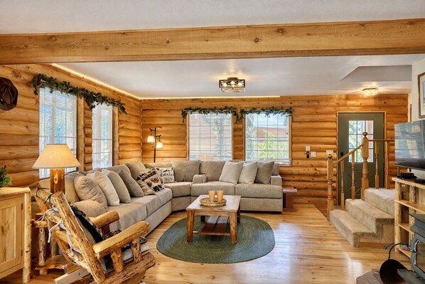 A cozy log cabin interior with a sectional sofa, a wooden coffee table, and a television on a wooden stand. - Blue Pine Forest Lodge 3 Bedroom Cabin (Leavenworth)