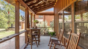 Une terrasse en bois avec une table et des chaises, un ventilateur de plafond et de grandes fenêtres donnant sur un jardin.