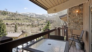 Ein Balkon mit Tisch und Stühlen, der auf eine gebirgige Landschaft mit Gebäuden in der Ferne blickt.