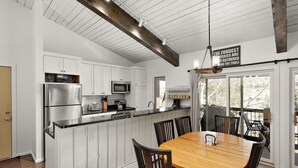 Eine Küche mit weißen Schränken, einem Edelstahl-Kühlschrank, einer Mikrowelle und einem Holzespeisetisch mit Stühlen.