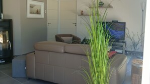 A modern living room with a beige sofa, a potted plant, a television, and a fireplace.