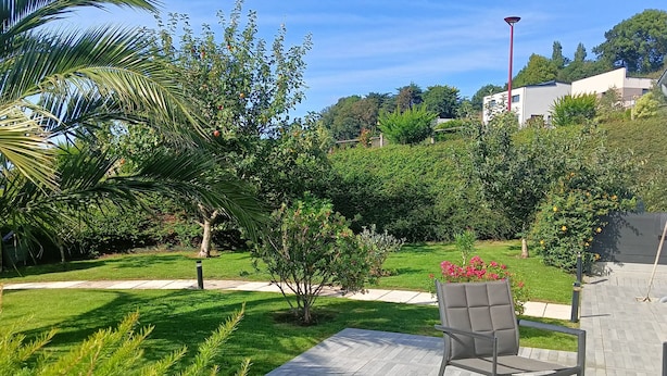 A patio area with a chair and a small table, surrounded by well-maintained grass and various shrubs.